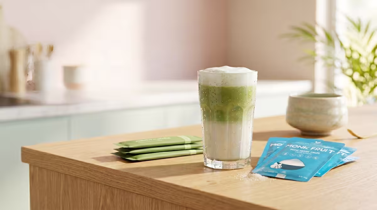 A refreshing creamy iced matcha latte in a tall glass next to natural monk fruit sweetener packets.